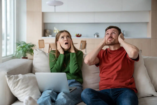 Couple on couch covering ears because of loud neighbor