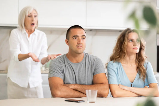 Older woman gesturing and complaining to a couple sitting with arms crossed at a kitchen counter.