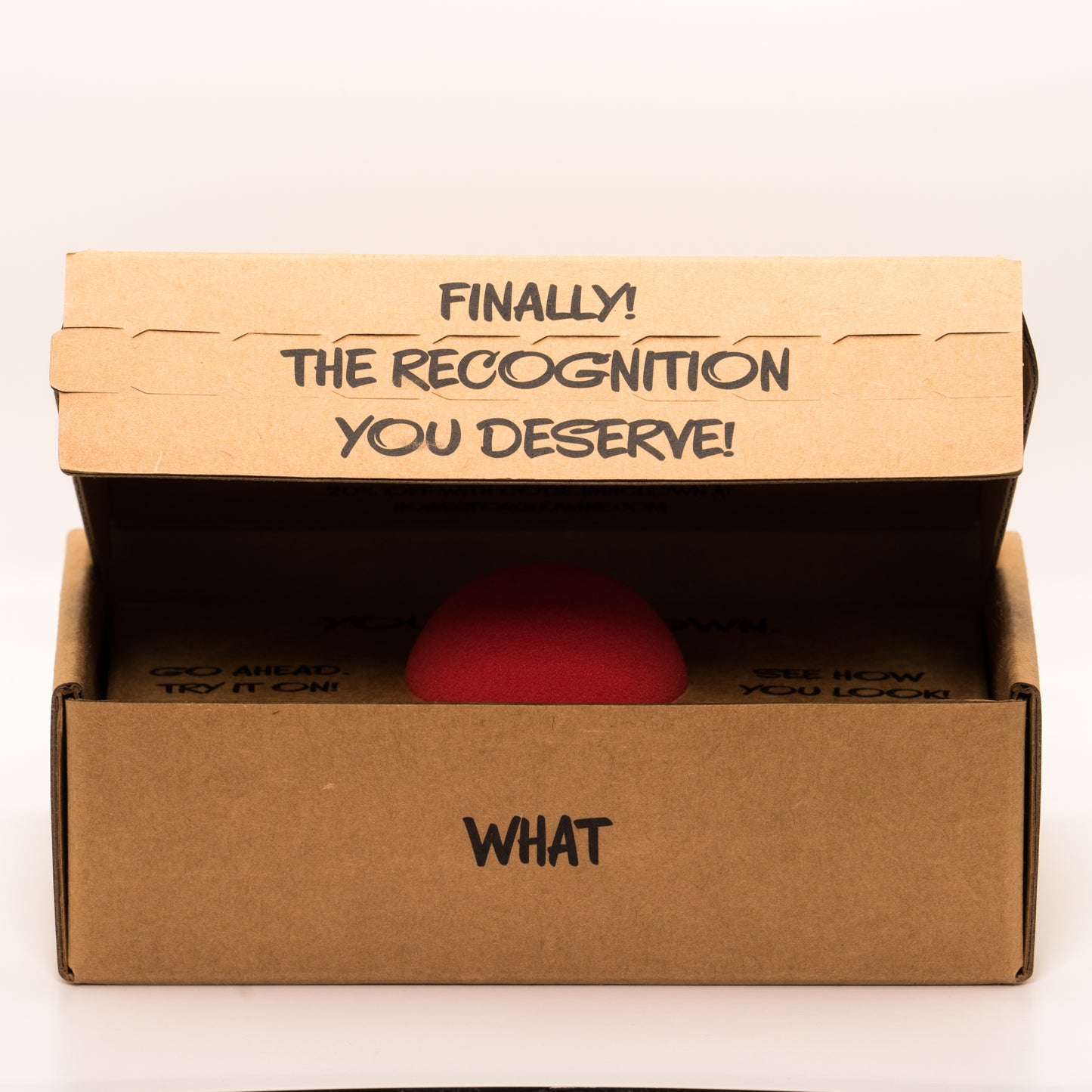 Partially open cardboard box with a red clown nose inside, with text “Finally the recognition you deserve!” on a white background.