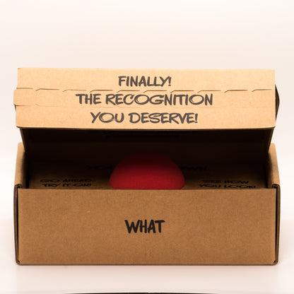 Partially open cardboard box with a red clown nose inside, with text “Finally the recognition you deserve!” on a white background.