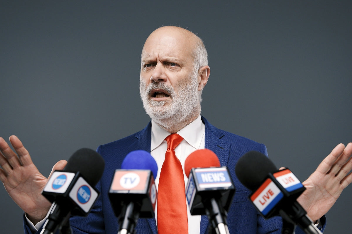 Corrupt clown politician shrugs at press mics in red tie—bald head, beard, and circus of excuses on full display!
